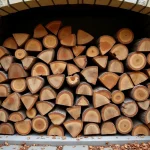 Stère de bûches de chêne empilées contre un mur en pierre d'une ferme française, comparatif poids bois de chauffage
